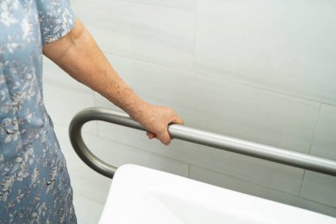 Asyalı yaşlı kadın hasta tuvalette tuvalet desteğini, tırabzan emniyet çubuğunu, hemşire hastanesinde güvenliği kullanıyor..