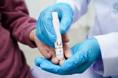 Diyabet tedavisinde kan şekeri seviyesini kontrol etmek için dijital glikoz ölçer kullanan Asyalı doktor.