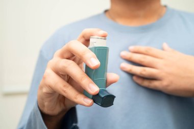 Astım ve kronik obstrüktif akciğer hastalığı COPD, Asyalı genç adam ölçülü doz solunum cihazı kullanıyor..