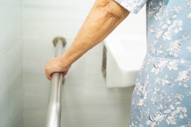 Asyalı yaşlı kadın hasta tuvalette tuvalet desteğini, tırabzan emniyet çubuğunu, hemşire hastanesinde güvenliği kullanıyor..