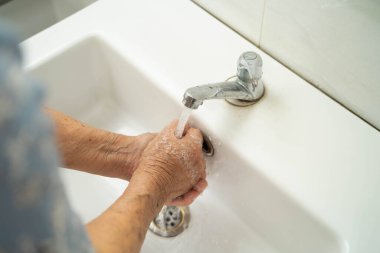 Asyalı yaşlı kadın banyoda ellerini yıkıyor..