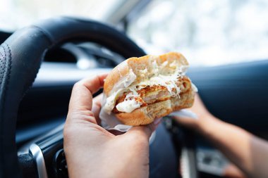 Asyalı kadın sürücü arabada hamburger yiyip, tutar, tehlikeli ve kaza riskini göze alır..