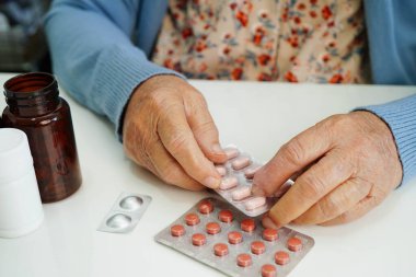 Asyalı yaşlı bir kadın elinde hap tutuyor, güçlü ve sağlıklı bir ilaç..