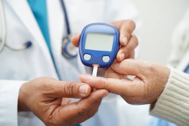Diyabet tedavisinde kan şekeri seviyesini kontrol etmek için dijital glikoz ölçer kullanan Asyalı doktor.