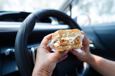 Asyalı kadın sürücü arabada hamburger yiyip, tutar, tehlikeli ve kaza riskini göze alır..