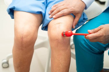 Asyalı doktor, hastanedeki yaşlı hastayı muayene etmek için diz refleksi sinirine vurdu..