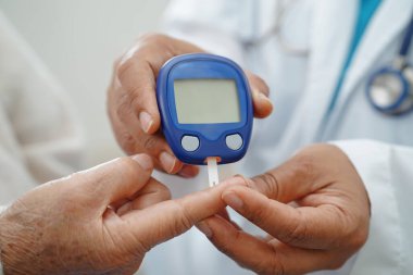 Diyabet tedavisinde kan şekeri seviyesini kontrol etmek için dijital glikoz ölçer kullanan Asyalı doktor.
