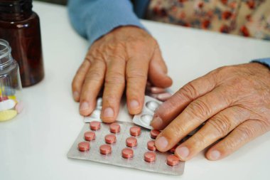 Asyalı yaşlı bir kadın elinde hap tutuyor, güçlü ve sağlıklı bir ilaç..