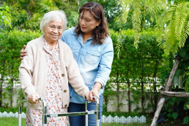 Bakıcı, Asyalı yaşlı kadın engelli hastaya parkta Walker 'la yürümesi için yardım ediyor..