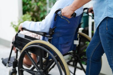 Bakıcı hastanede tekerlekli sandalyede oturan Asyalı yaşlı kadın maluliyet hastasına yardım ediyor..