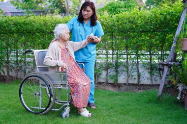 Doktor, Asyalı yaşlı kadın engelli hastaya parkta yürüme konusunda yardım ediyor..