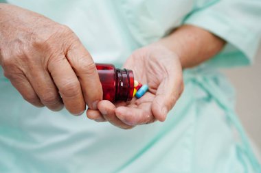 Asyalı yaşlı kadın elinde hap kapsülü ilacı tutuyor..