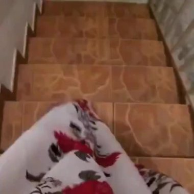 Uzun baskılı bir elbise giymiş bir insan merdivenden aşağı iniyor ve gölgesi loş ışıkta, elinde bir kamerayla yansıyor..