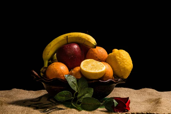 stock image still life of fruits bananas oranges lemons apples on a clay pot on a dark background