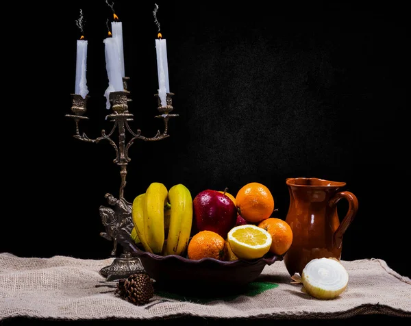 stock image still life of fruit on a clay vase with a candle holder on a dark background