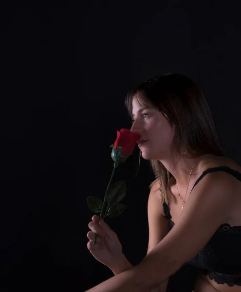 黒いドレスを着た美しい若い女性が黒い背景に赤いバラを手に — ストック写真