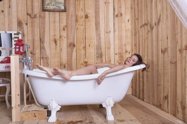 一个漂亮的女人躺在一个白色的旧浴缸里 手里拿着一杯饮料放松地休息着 — 图库照片