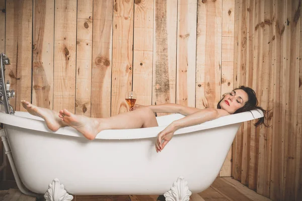 一个漂亮的女人躺在一个白色的旧浴缸里 手里拿着一杯饮料放松地休息着 — 图库照片