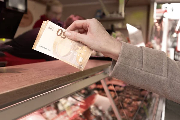 A woman stands at the counter and holds a euro banknote in her hands to pay for the goods. High quality photo