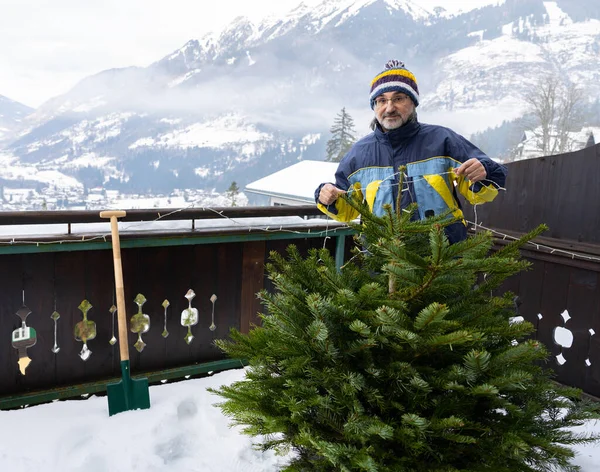 Uzun saçlı, parlak ceketli ve şapkalı yetişkin bir adam balkondaki Noel ağacını süslemeye hazırlanıyor. Yüksek kalite fotoğraf