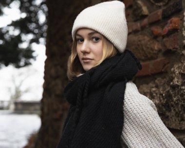 Eski bir tuğla duvarın arka planında yumuşak, kalın giysiler giymiş bir kızın portresi. Yüksek kalite fotoğraf