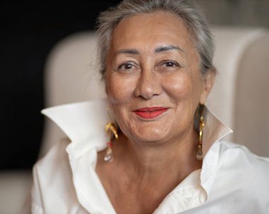 Charming lady in a loose white shirt with a hairstyle looks at the camera and smiles. High quality photo