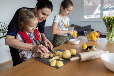 A mother and two daughters cook apple pie filling together at the table, a mother teaches her daughter to crumble apples. High quality photo