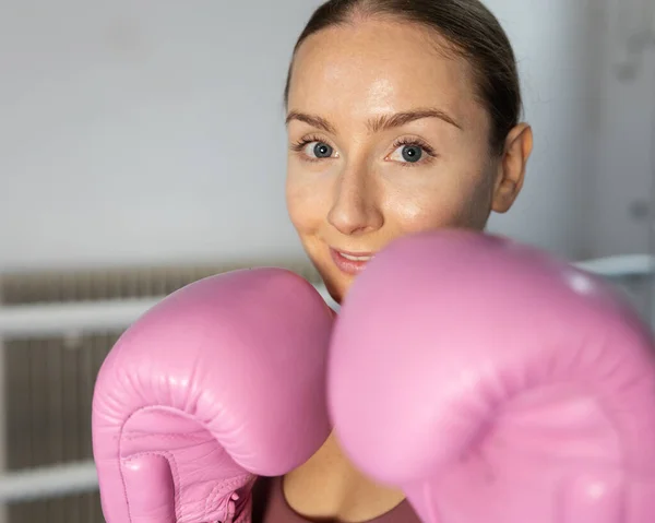 The girl stands in a boxing pose in pink gloves and smiles at the camera. High quality photo