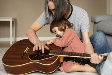 Küçük bir kız yerde oturan büyükbabasının gitarına ilgiyle bakıyor. Yüksek kalite fotoğraf