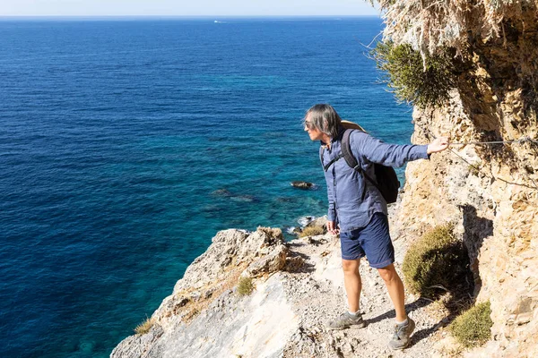 Stock image A man stands on a rock trail and looks down at the sea, Greece, Crete. High quality photo