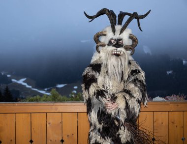 Krampus, Noel efsanelerinin kahramanı, deri ve boynuzlu bir maske giymiş, sis, Avusturya ve Gastein 'in arka planına karşı tahta bir çitin önünde duruyor. Yüksek kalite fotoğraf