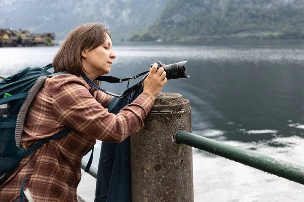 Sırt çantalı bir kadın turist bulutlu havada büyük bir gölün fotoğraflarını çekiyor, açık hava eğlencesi kavramı, Hallstatt, Avusturya. Yüksek kalite fotoğraf