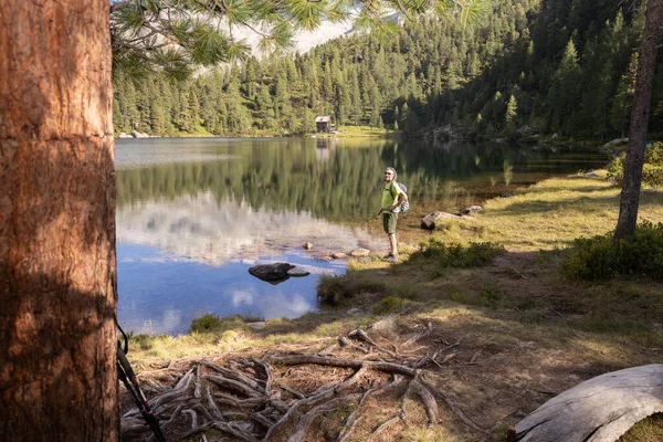 Stock image A man with a backpack stands on the shore of a beautiful lake with a reflection among a coniferous forest: Austria. High quality photo