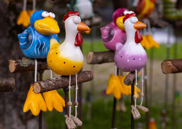 Bright ceramic toy birds sitting on wooden perches are sold at the street market. High quality photo