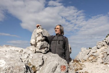 Yüzünde bir gülümseme olan gri saçlı, uzun saçlı bir adam Avusturya 'da farklı boyutlarda taşlardan bir kule inşa ediyor. Yüksek kalite fotoğraf