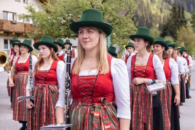 Geleneksel dirndl elbiseler ve yeşil şapkalar giyen bir grup kadın Alplerdeki bir dağ köyünde geçit töreninde enstrüman çalıyor. Kadınlar sırada, her biri bir müzik aleti tutuyor.. 
