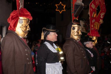 Geleneksel giysiler ve süslü maskeler giyen bir grup insan gece yürüyüşü sırasında bir geçit töreninde yürürler..