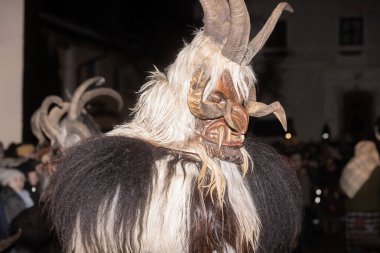 Geleneksel boynuzlu ve uzun beyaz kürklü bir maske takan bir insan gece yürüyüşü sırasında kalabalığın içinden geçer..