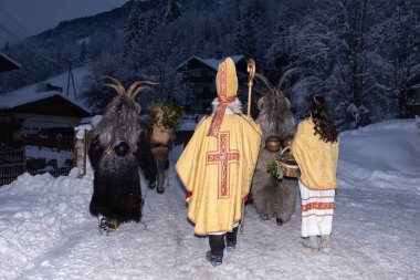 Bu resim, Avusturya 'da karlı bir köyde yürüyen bir grup Krampus figürünü gösteriyor. Rakamlar geleneksel Krampus kostümleri giyiyorlar, boynuzları, kürkü ve çanları var.. 