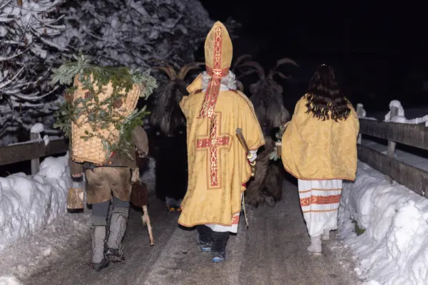 Bu resim, Avusturya 'da karlı bir köyde yürüyen bir grup Krampus figürünü gösteriyor. Rakamlar geleneksel Krampus kostümleri giyiyorlar, boynuzları, kürkü ve çanları var.. 