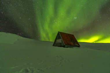 İzlanda 'nın güzel Aurora Borealis' inde karanlık bir gökyüzünün altında bir dağ geçidinde sığınma kabini.