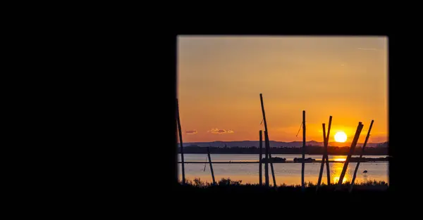 漁小屋の窓からカマルグの池の夕日を見る 保護された自然保護区 ロイヤリティフリーのストック写真