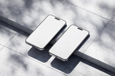 Beton arka planda beyaz ekranlı iki telefon.