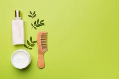 Shampoo and mask with herbal extract and comb on color background, top view.