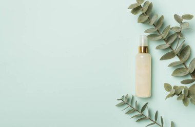 Renkli arka planda okaliptüs dallı kozmetik şişesi, üst görünüm.