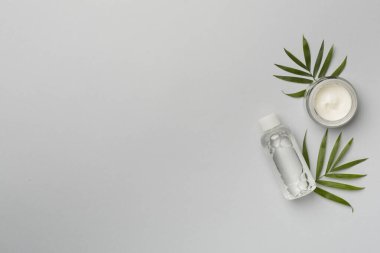 Renkli arka planda yeşil yapraklı yüz toniği ve kremi, üst görünüm.