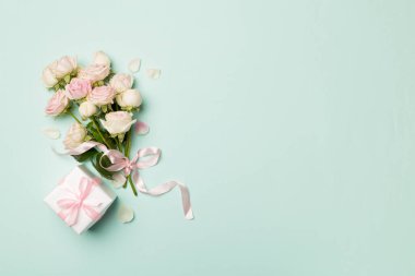 Gift box and rose flowers on color background, top view