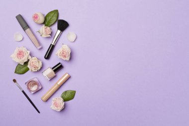 Makeup products with flowers on color background, top view.