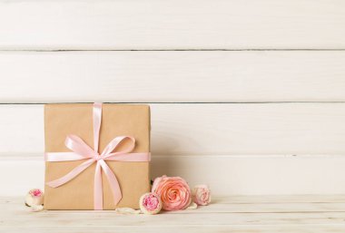 Gift box with pink rose flower on light table.