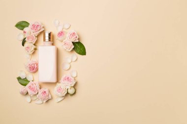 Cosmetic bottle with rose flower on color background, top view.